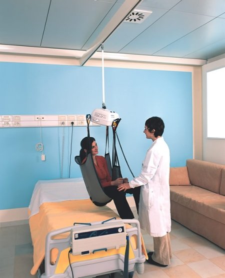 assistente imbraga sul sollevatore una utente sul letto