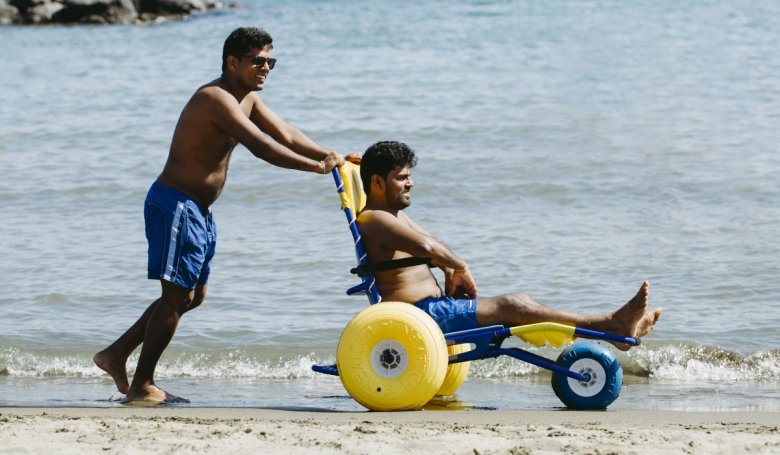 un uomo su una piaggia spinge un ragazzo seduto sulla sedia job