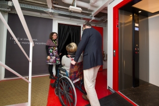 signora in carrozzina entra accompagnata in un percorso per ciechi a scopo educativo