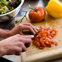 primo piano su mani che tritano un pomodoro con un coltello sopra un tagliere di legno