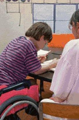 bambina in carrozzina di spalle fa i compiti vicino a una donna che la aiuta