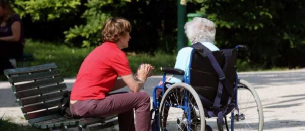 una badante vicino ad un'anziana in carrozzina in un parco