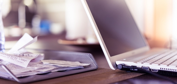 scrivania su cui sono appoggiati un computer portatile acceso ed un raccoglitore con all'interno molti scontrini