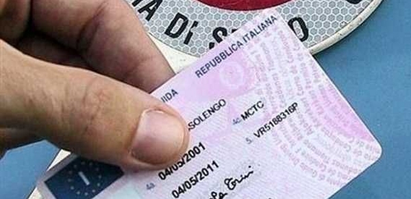 uomo tiene in mano una patente in formato tessera con una paletta della polizia sullo sfondo