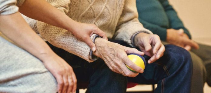 anziano che tiene in mano una pallina e una persona gli tiene la mano
