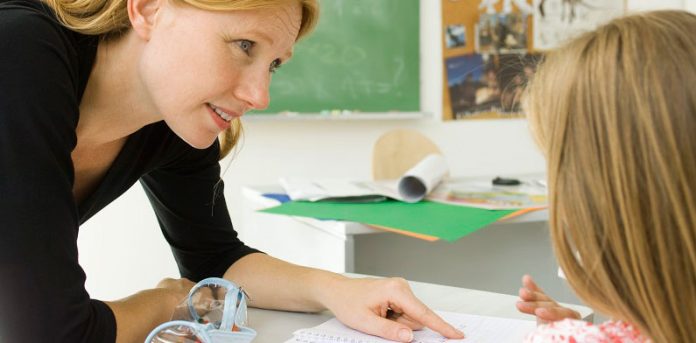 una maestra sta indicando ad una bambina dove leggere sul quaderno