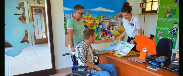 una ragazza al desk mostra una mappa del parco ad un ragazzo in carrozzina e suo padre