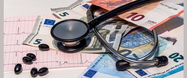 uno stetoscopio sopra dei soldi di carta e di moneta e delle pillole di lato