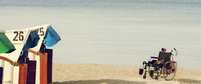 sedia a rotelle sulla spiaggia con mare sullo sfondo e spogliatoi a lato