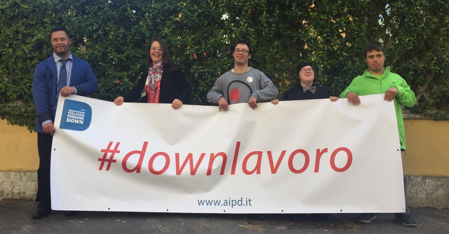 ragazzi down che tengono in mano uno striscione con l'hashtag #downlavoro
