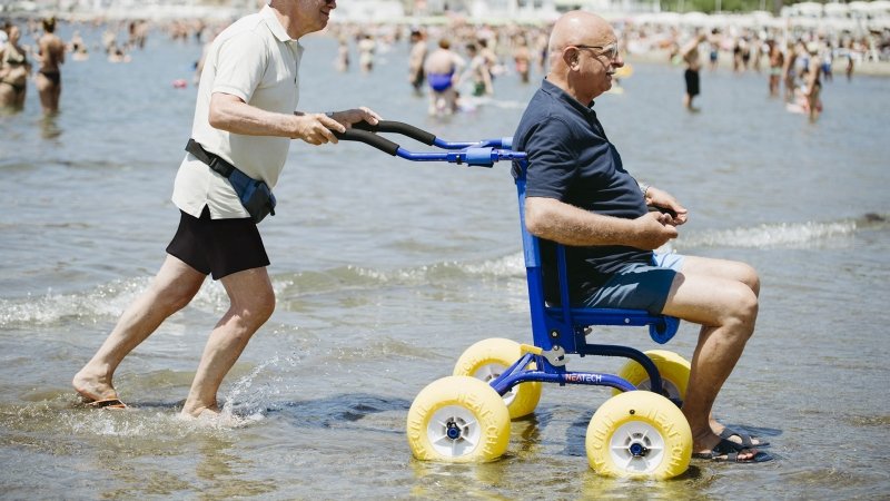 persona spinge un uomo seduto sul deambulatore da spiaggia jobwalker