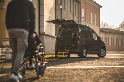 persona di spalle spinge una carrozzina verso un doblo con portellone aperto, olmedo per trasporto di passeggeri disabili