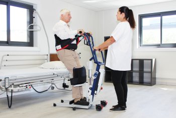 anziano sollevato dal letto da parte di una operatrice, con l'aiuto di un verticalizzatore