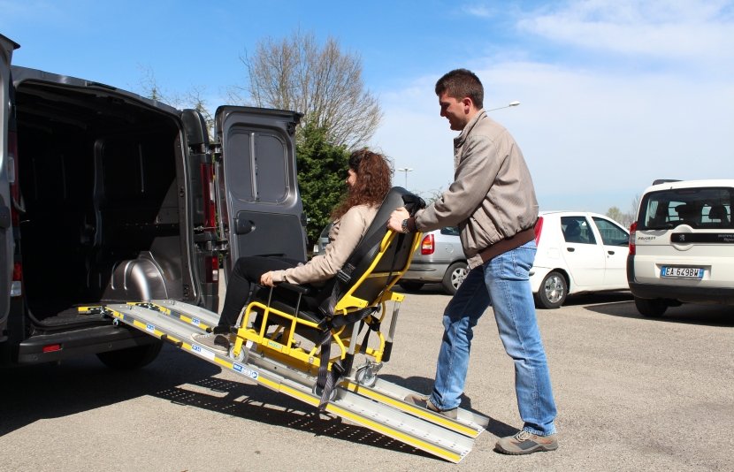 ragazza in carrozzina viene spinta in auto su rampe telecopiche per il dislivello dal suolo ala macchina