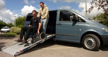 uomo fa scendere dall'auto un passeggero in carrozzina attraverso una rampa sabili auto carrozzina