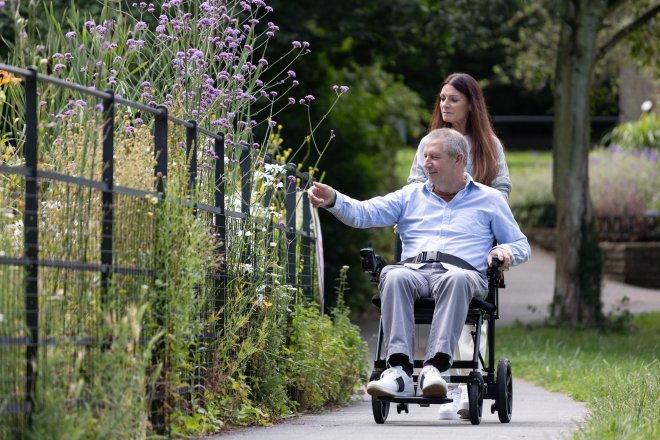 uomo seduto su carrozzina elettrica guidata da una caregiver