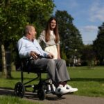 uomo in carrozzina passeggia a fianco ad una donna