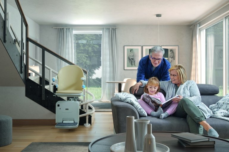 salotto con nonni sul divano con nipotina, e sullo sfondo montascale a poltroncina installato su scala