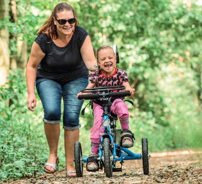 bambina  a bordo del suo triciclo, vicino a una donna adulta, in un parco