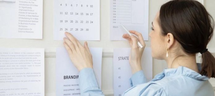 donna di spalle mentre scrive du un calendario appeso alla parete