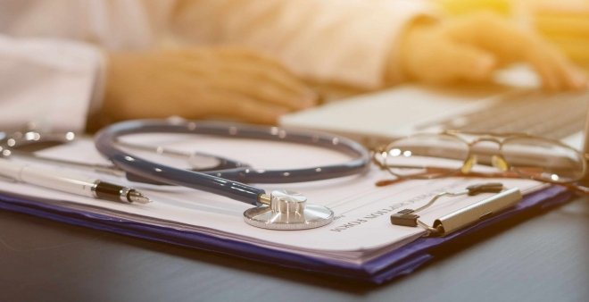 piano di una scrivania sulla quale c'è uno stetoscopio, un pc e alcuni documenti