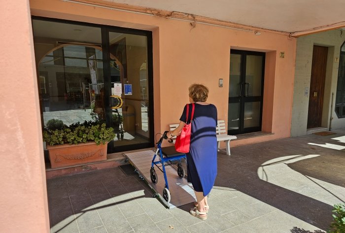 donna con un deambulatore passa sopra ad una rampa d'accesso posta sopra alcuni gradini, per accedere ad un negozio