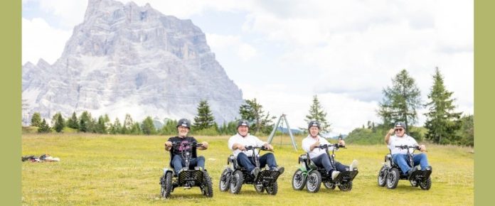 su un pianoro con montagne alle spalle, quattro persone a bordo di Zoom il quad per disabili