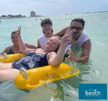 signora in mare con salvagente, circondata da alcuni ragazzi del progetto spiaggia accessibile, nel  mare del  salento