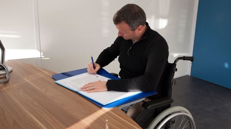 uomo in carrozzina scrive sul piano da appoggio aggiunto al tavolo