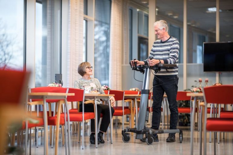 uomo in un ristorante tra i tavoli si muove appoggiandosi ed utilizzando un deambulatore con supporto per avambracci