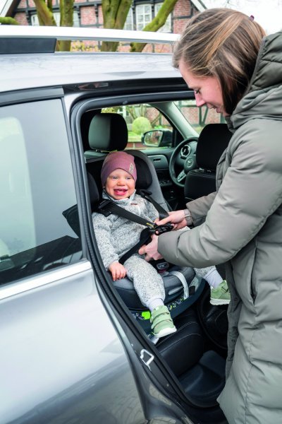 donna aggancia le cinture di sicurezza di un seggiolino auto sul quale è seduto un bambino