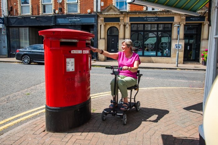 signora anziana in città su uno scooter mentre imbuca una busta nella cassetta delle lettere