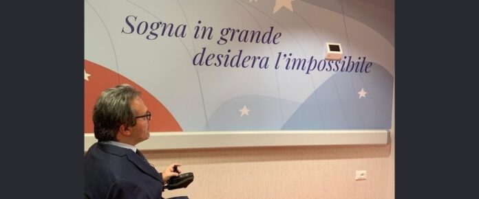 Alberto Fontana civino alla scritta diuna parete di un Centro NEMO che recita: Sogna in grande, desidera l'impossibile