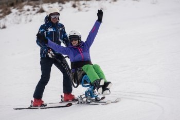 ragazza sulle piste da sci seduta sul DualSki, guidato da un accompagnatore alle sue spalledualski disabili