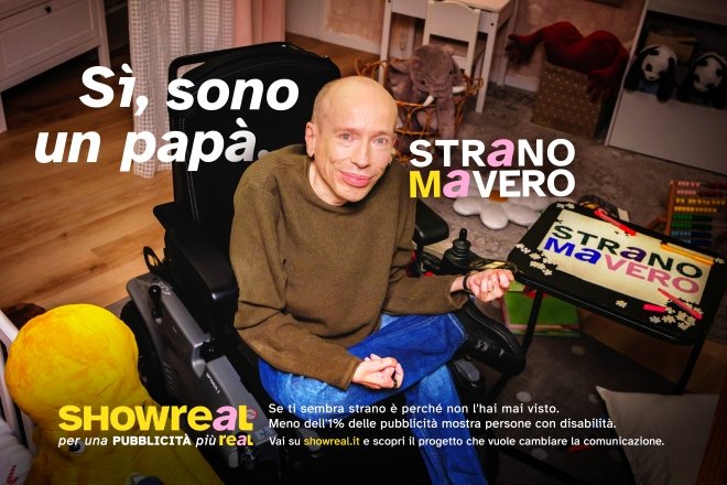 Max Ulivieri, sulla sua carrozzina, in un ambiente domestico. La scritta sulla foto dice: Sì, sono un papà. Strano ma vero