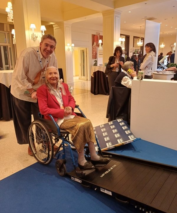 un uomo spinge una donna anziana sulla carrozzina vicino ad una rampa WM System in esposizione in fiera