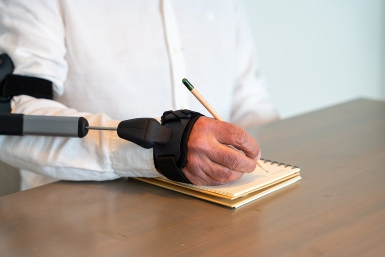 dettaglio della mano di una persona che scrive mentre indossa la ortesi STIL anti tremori