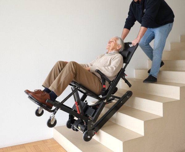 uomo utilizza un montascale a cingoli per far superare una scala ad  un anziano in carrozzina