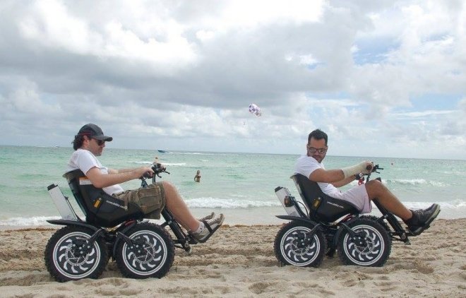 due ragazzi sul bagnasciuga di una spiaggia si muovono usando i quad per persone disabili Zoom